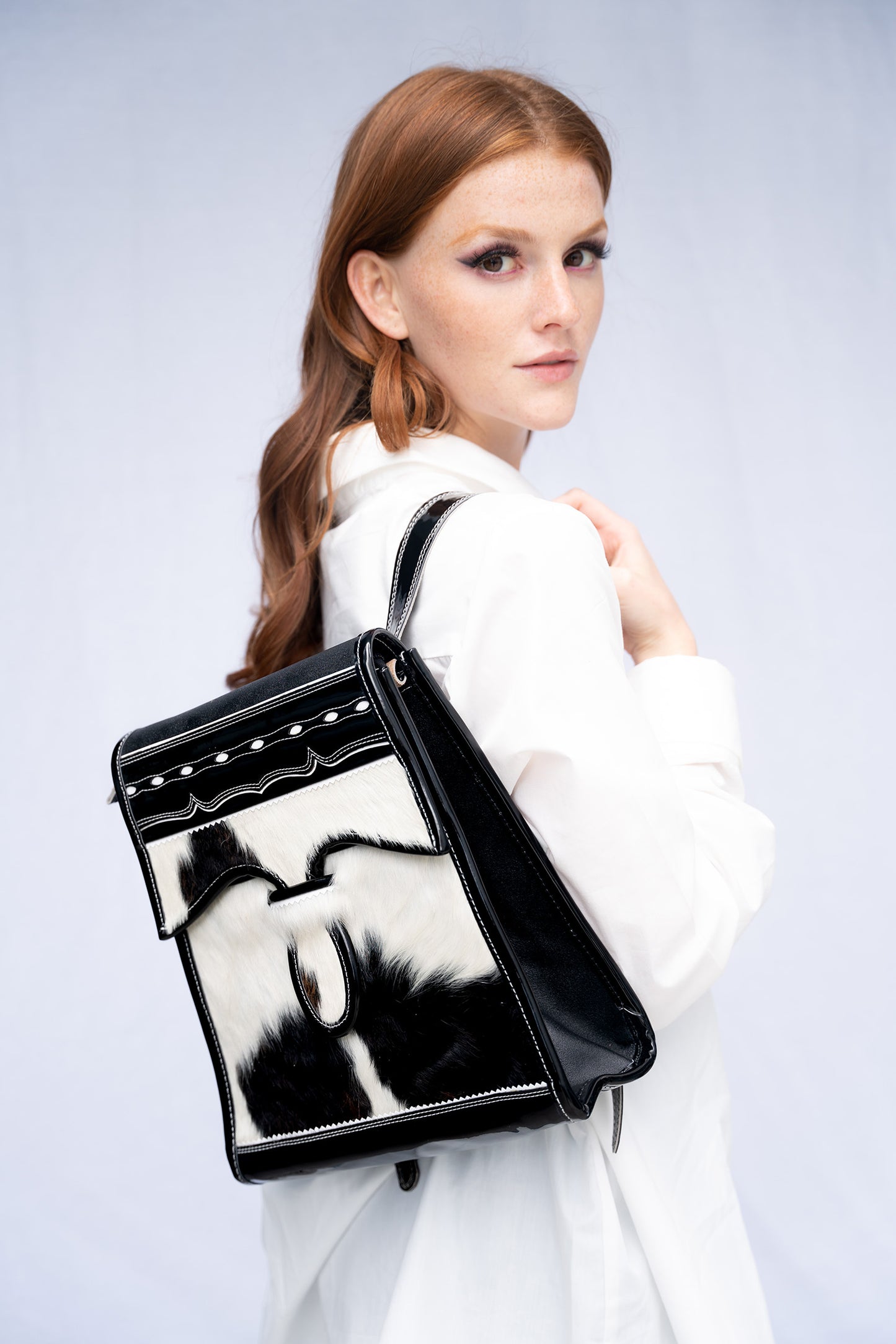 Woman holding a black and white leather cowhide handbag against a light gray background
