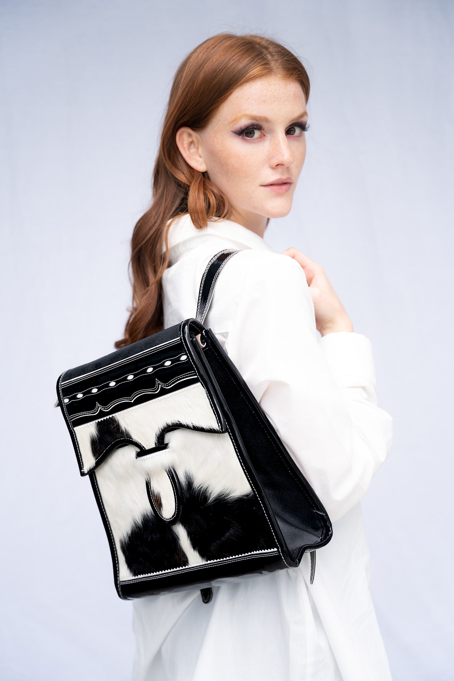 Woman holding a black and white leather cowhide handbag against a light gray background