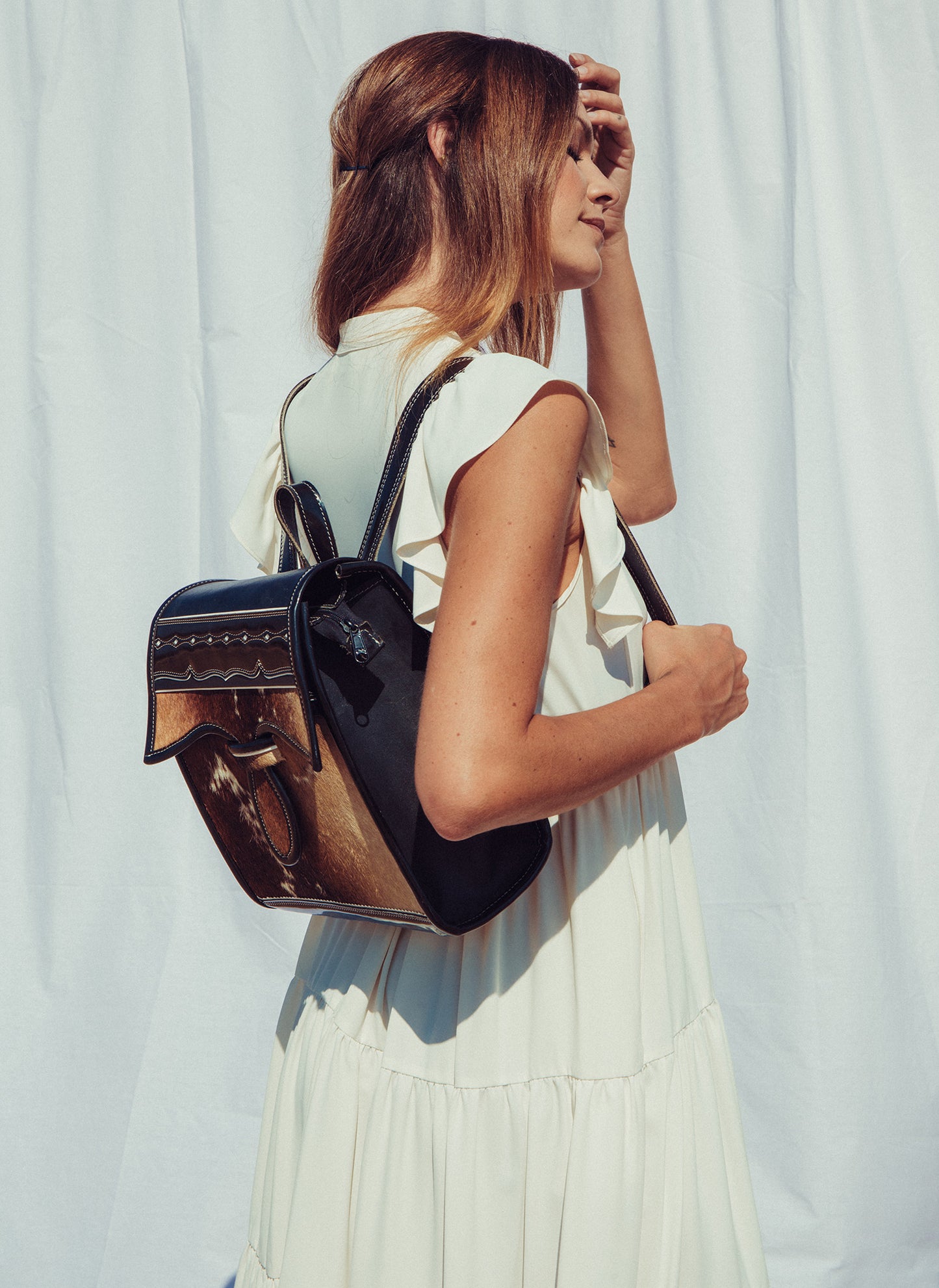 Woman holding a black and brown leather backpack against a light background